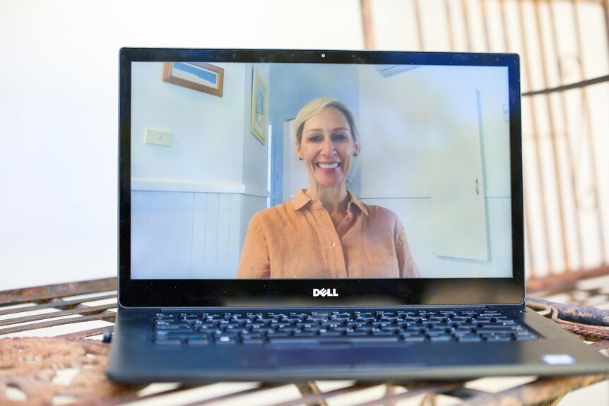 A woman in an orange shirt on a laptop screen.