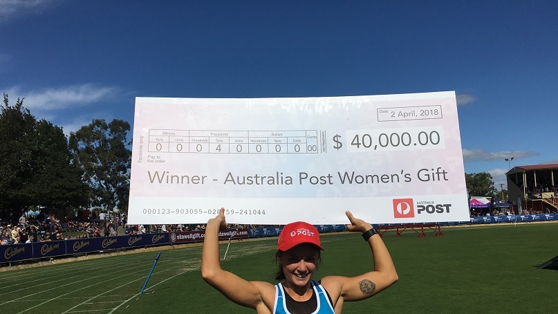 A young woman holds an oversized winner's cheque after winning the Stawell Gift women's final