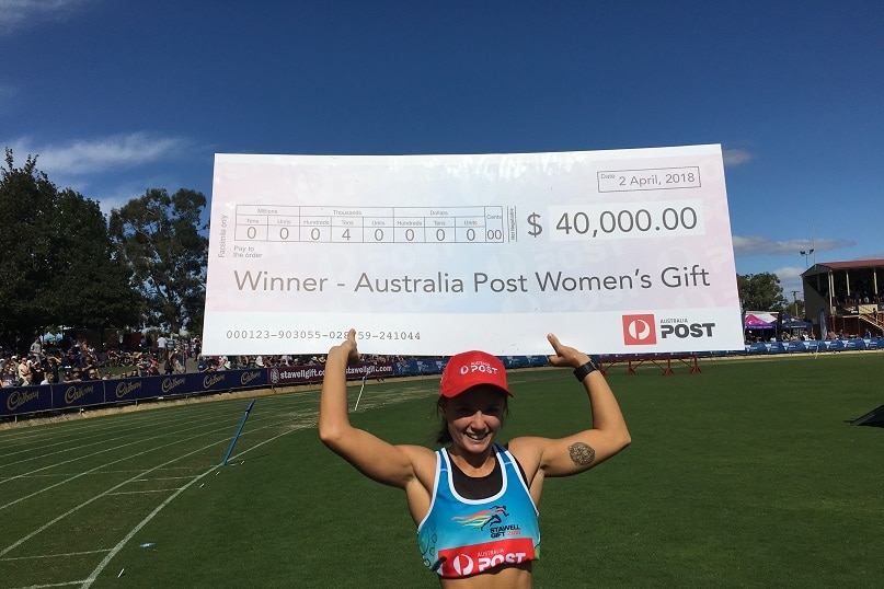 A young woman holds an oversized winner's cheque after winning the Stawell Gift women's final