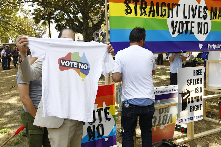 people at a rally in 2017 protesting against the same-sex marriage plsebistice, a man can be seen holding a t-shirt with vote no