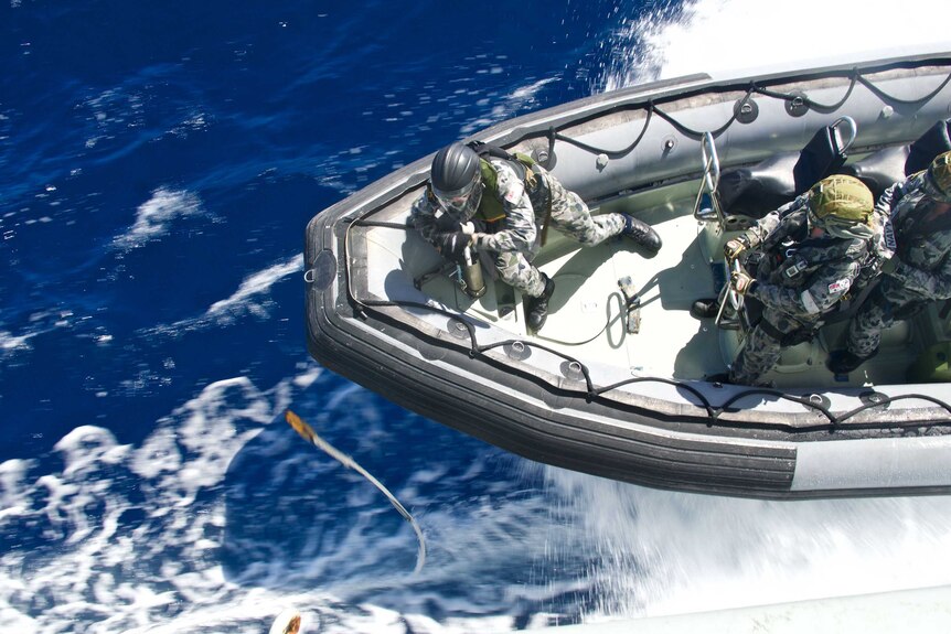 Three sailors are seen from overhead, on board a fast-moving inflatable craft.