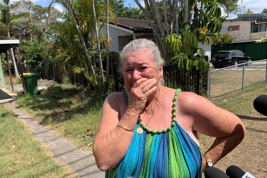 Woman holds hand to mouth crying outside the home where the girls died.