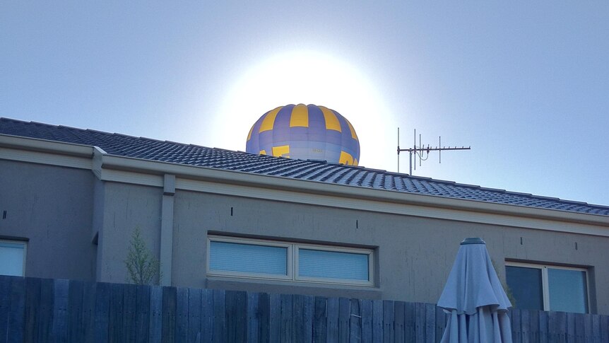 A hot air balloon appears over the roof of a house.