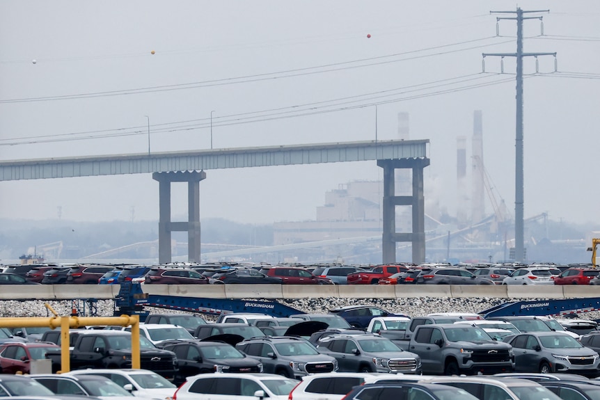Cars are parked in rows in the foreground. The ramp to the missing bridge is seen behind them.