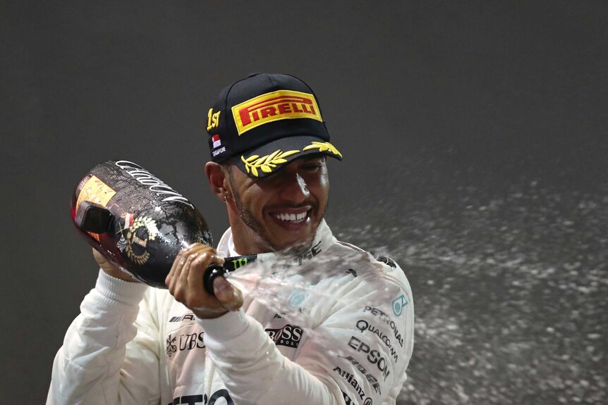 A smiling Lewis Hamilton sprays champagne on the winner's podium.