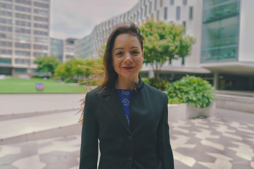 Law professor Thalia Anthony standing and smiling at the camera,  with high-rise buildings in the background.