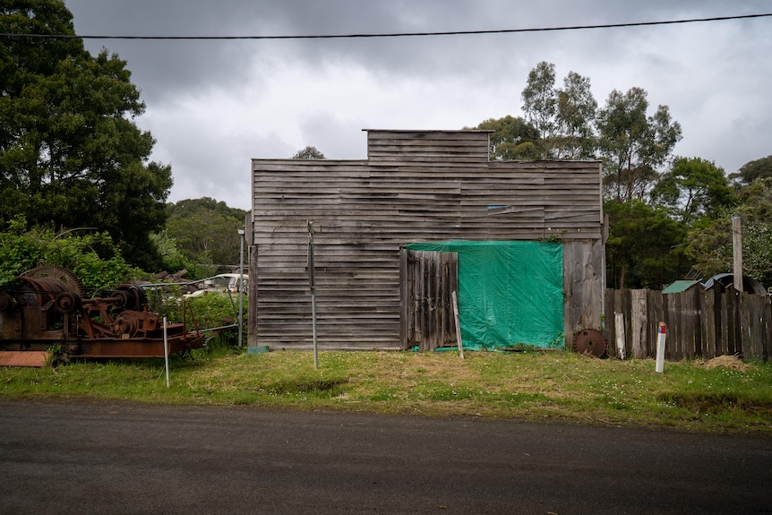 An old timber shed missing a door faces a street.