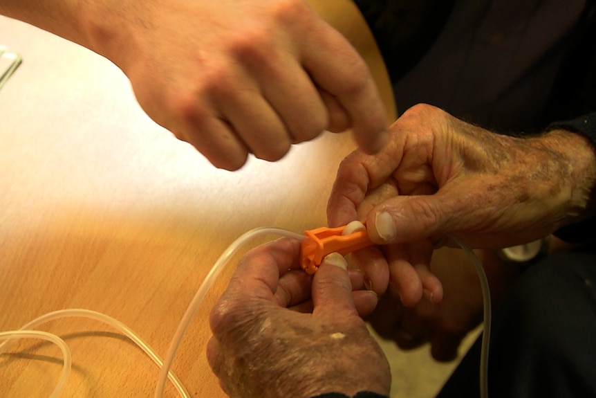 Close up of David Goodall's hands on a tube covered in a clamp. Another hand points to part of the clamp.