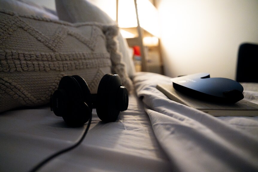 A dimly lit room with a bed and two couches next to it, with a pair of headphones on the bed.
