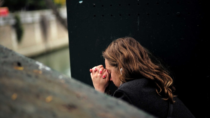 A woman prays by a river in Paris