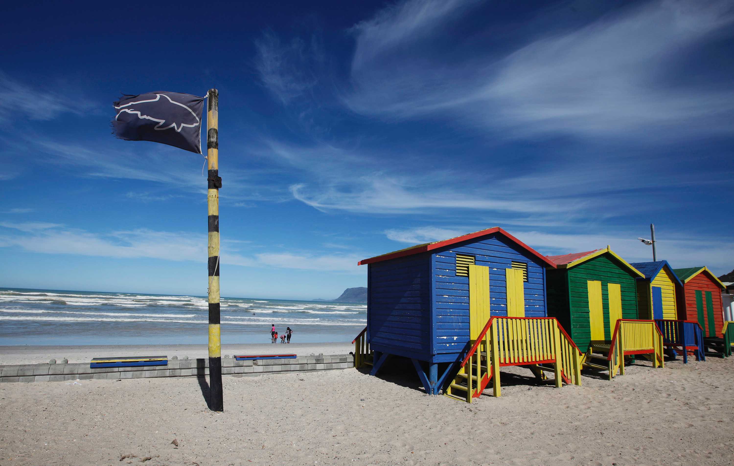 A black flag with the outline of a shark near colourful beach huts.