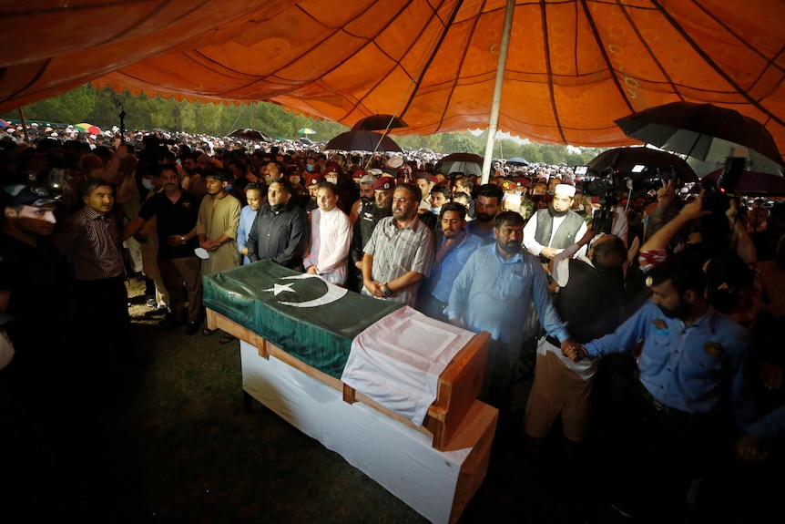 A crowd of people surround a coffin draped in the Pakistani flag. 