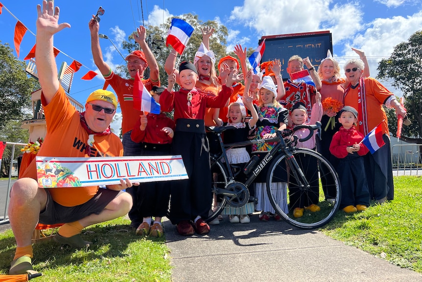 Un groupe d'hommes, de femmes et d'enfants qui chantent, vêtus d'orange, tenant des drapeaux néerlandais et un drapeau néerlandais, se tiennent debout sur une bicyclette.