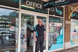 A man stands in front of an office supplies shop