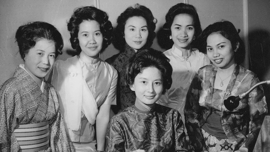 A photo of female Radio Australia announcers in the 1960s. Some wear traditional clothing, one woman is holding a vinyl record.