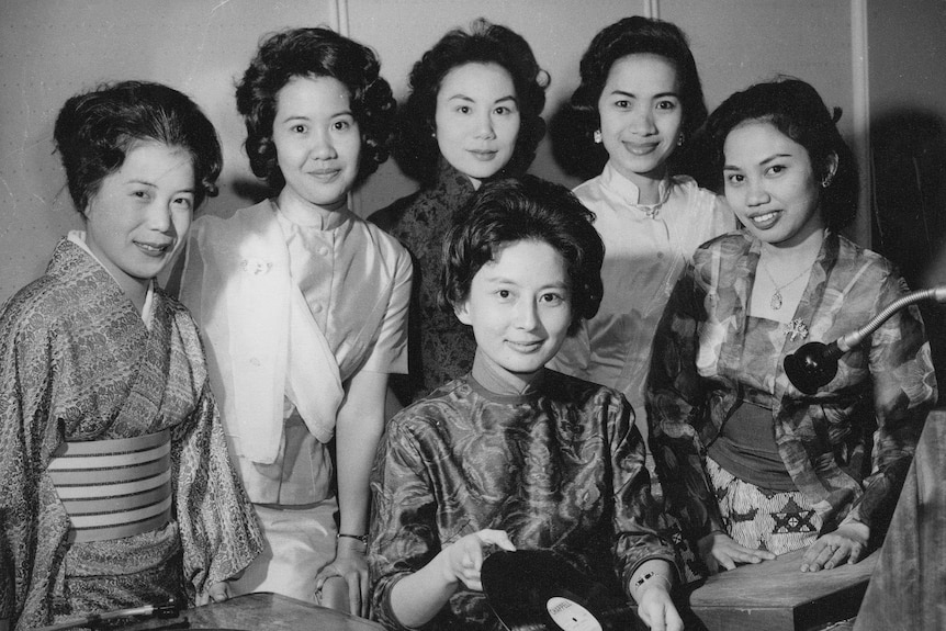 A photo of female Radio Australia announcers in the 1960s. Some wear traditional clothing, one woman is holding a vinyl record.