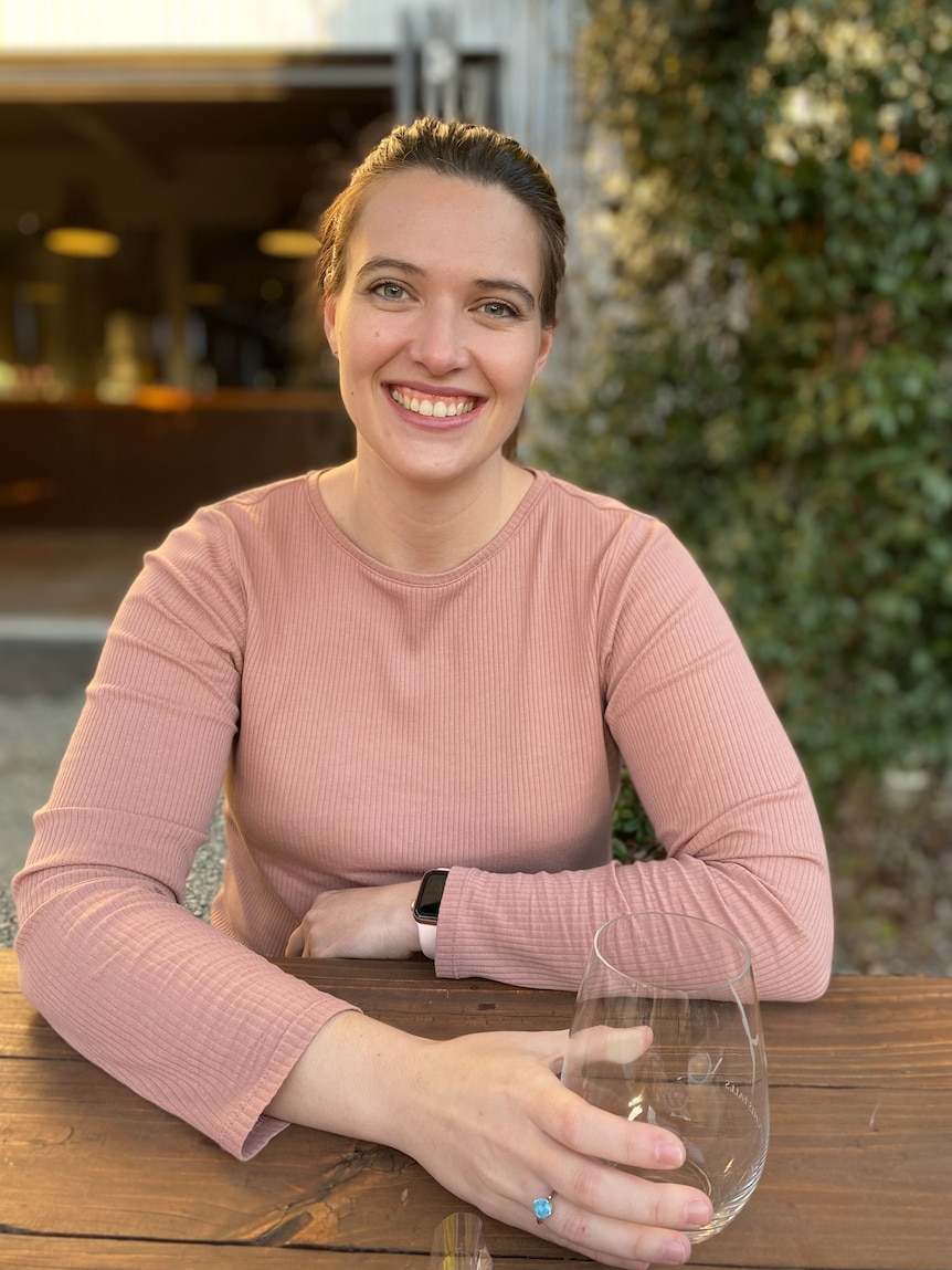 Shae sitting at an outdoor table, holding a drink and smiling.