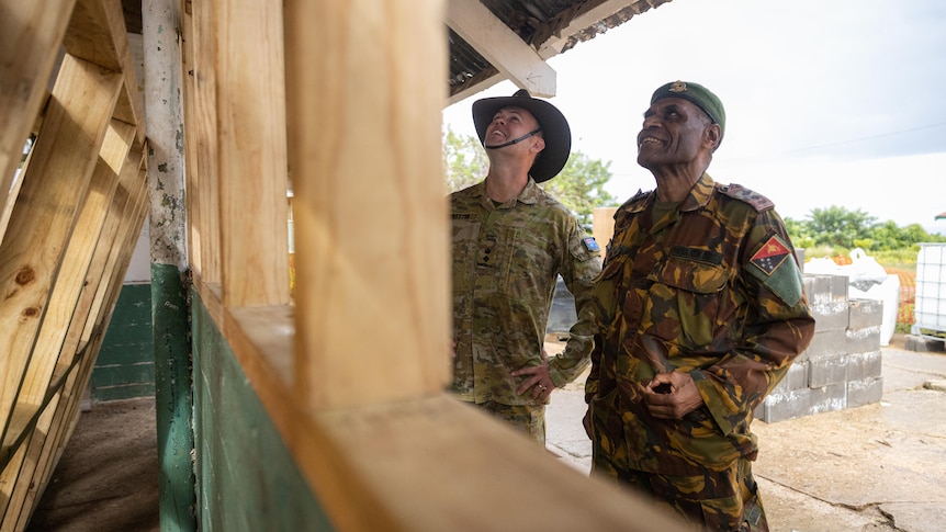 Two men in military uniforms inspect a half-built classroom. 