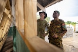 Two men in military uniforms inspect a half-built classroom. 