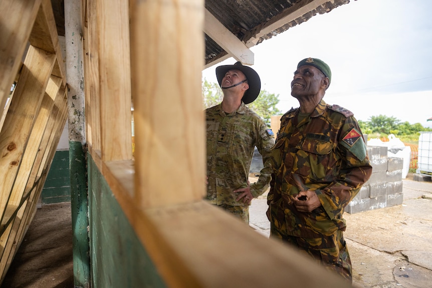 Two men in military uniforms inspect a half-built classroom. 