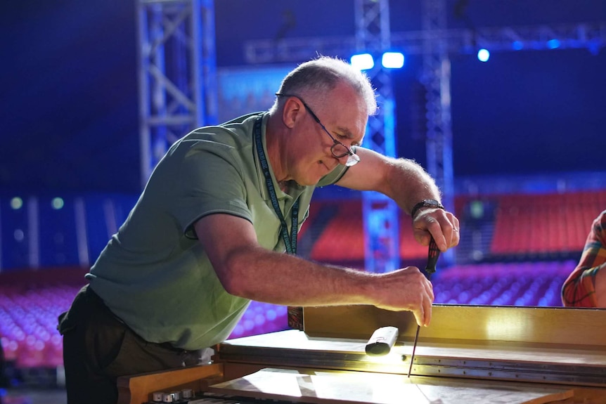 A man with glasses leans over an organ with a screwdriver.