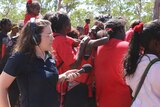 Woman with headphones on and a microphone recording a group of Indigenous people with bush in the background.