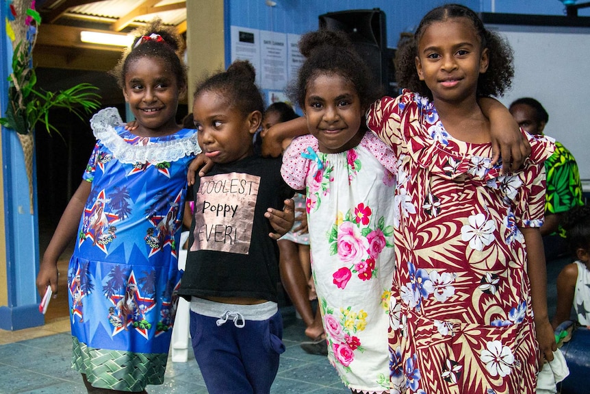 Four young girls in bright dresses smiling to the camera.