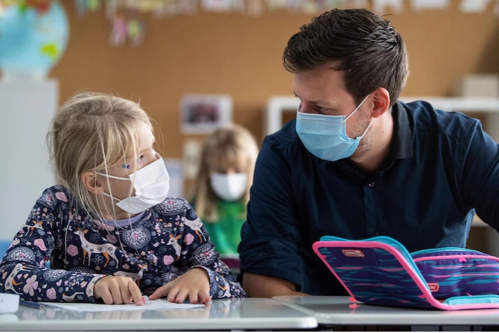 A teacher wearing a mask looks at a student who also wears a mask.