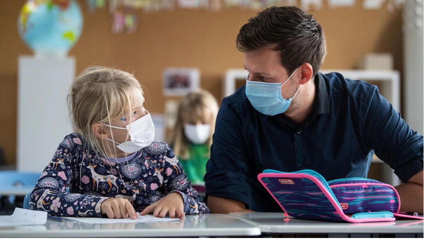 A teacher wearing a mask looks at a student who also wears a mask.