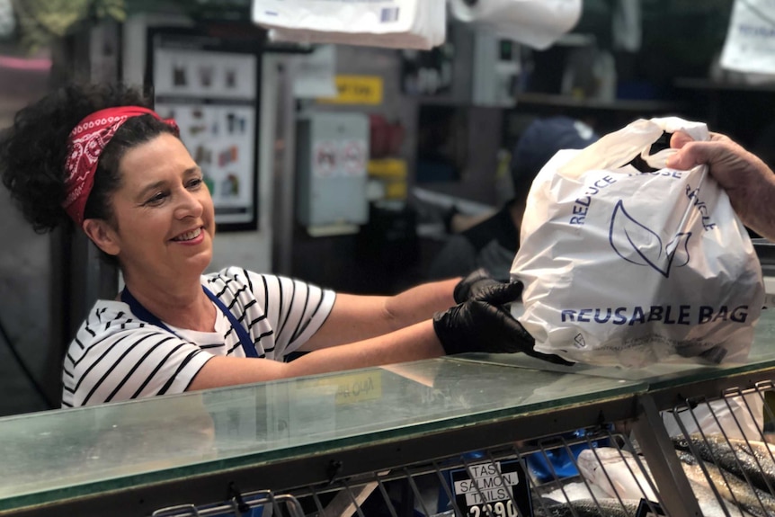 Lisa Sheppard hands a reusable shopping bag to a customer at a fish monger shop.