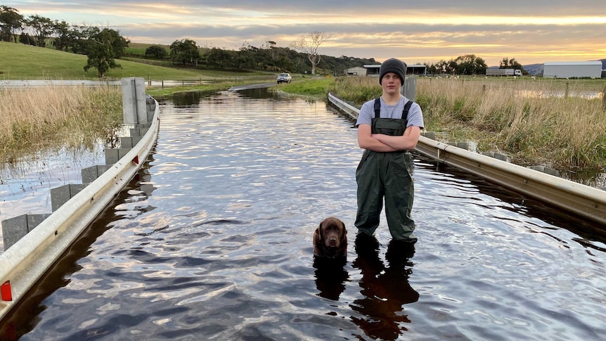 A teenage boy and his labrador dog stand on a flooded road in the Aire Valley.