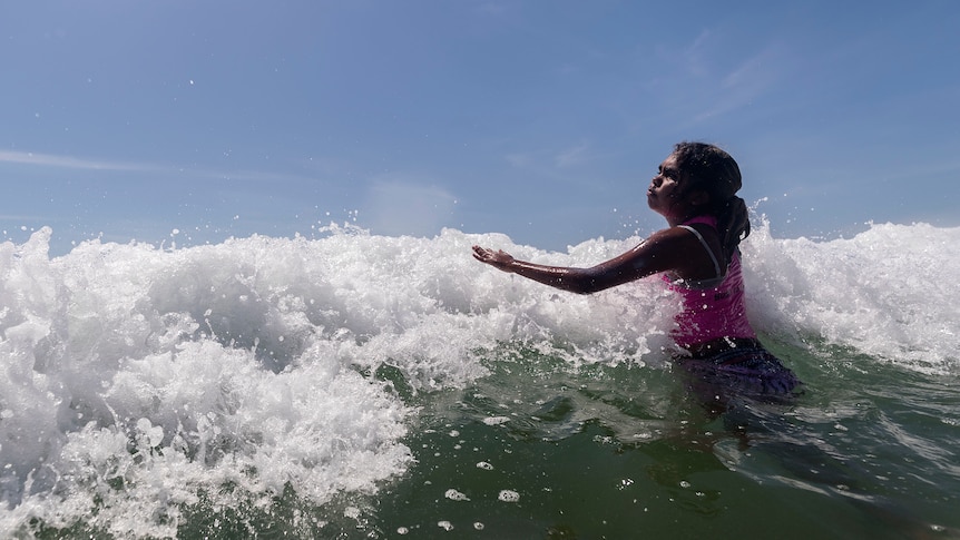 An indigenous Australian girl swims against the waves in the ocean.