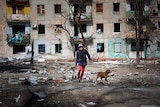 A man walking with a dog in a ruined area near Mariupol. 
