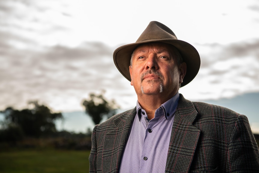 A man looks out into the distance, with trees and the sky behind him.