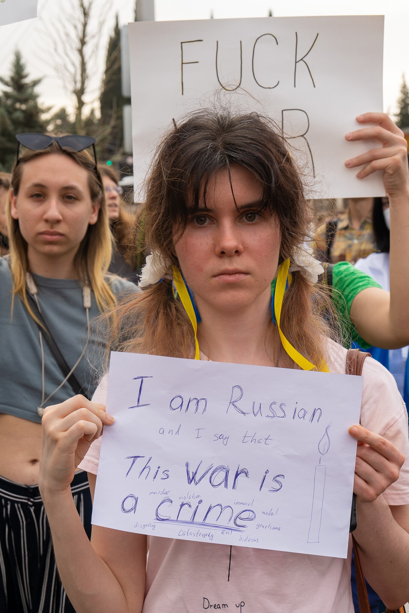 A young woman holds a sign reading 'I am Russian ... this war is a crime'.