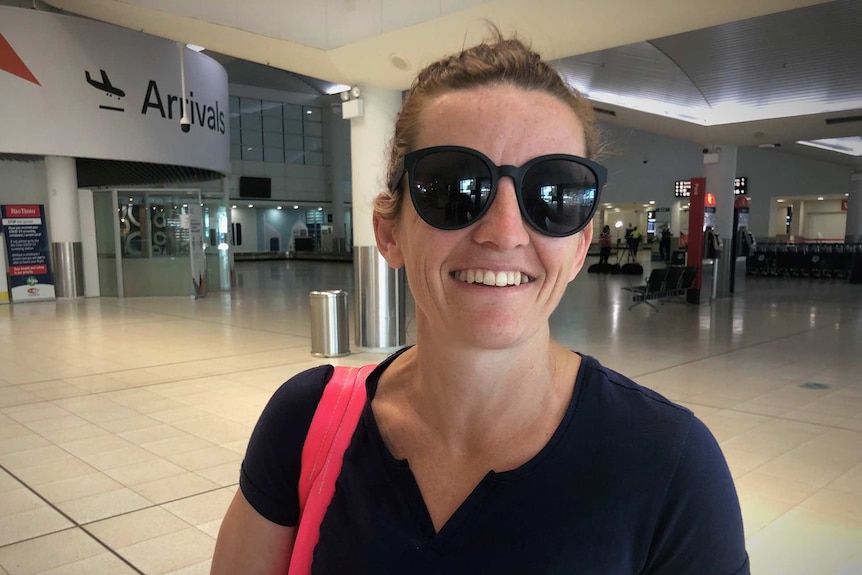 A woman in sunglasses and holding a bag stands in an airport terminal