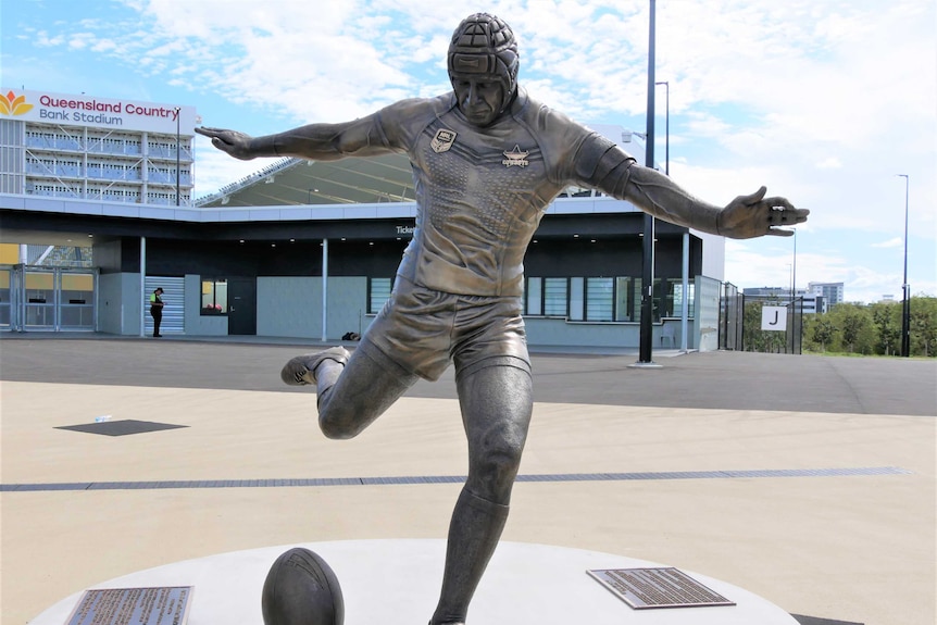 A bronze statue of NRL player Johnathan Thurston kicking a football with his arms outstretched.
