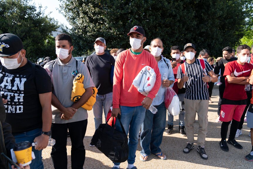 Young men in caps wearing masks hold blankets and belongings on a Washington street.
