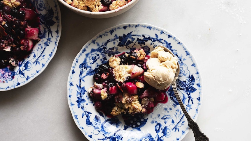 A serving of pear and blueberry crumble on a plate with a scoop of ice cream for a seasonal spring dessert recipe.