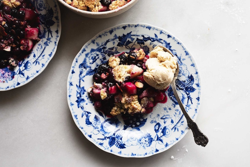 A serving of pear and blueberry crumble on a plate with a scoop of ice cream for a seasonal spring dessert recipe.
