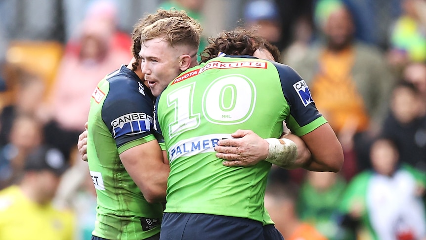 Three Canberra Raiders NRL players embrace as they celebrate a try against Wests Tigers.