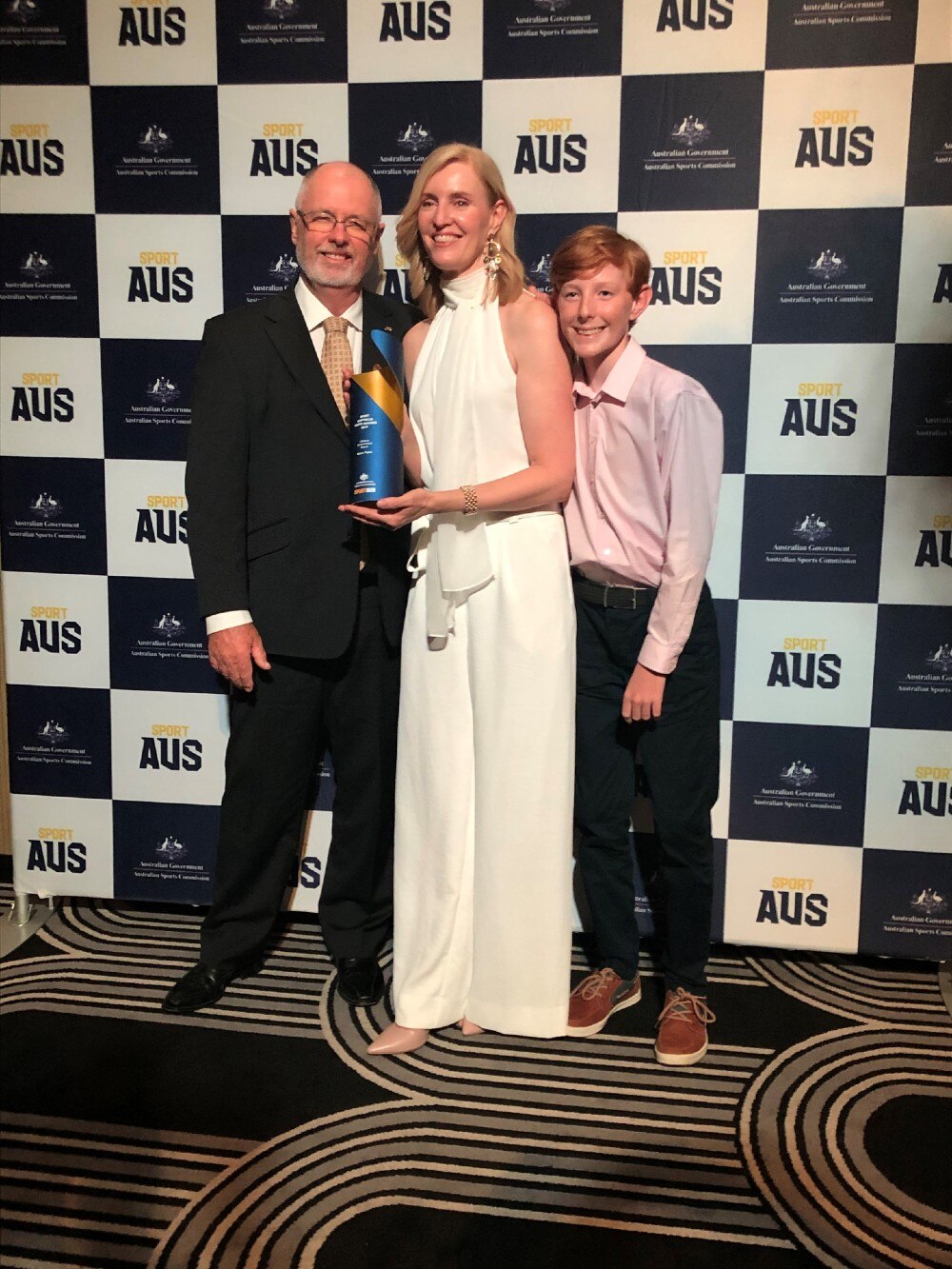 A woman holding a trophy with a man and child either side of her.