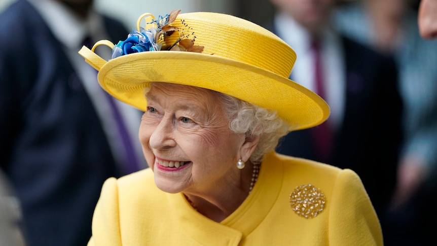 Queen Elizabeth II smiles wearing a yellow hat and coat