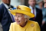Queen Elizabeth II smiles wearing a yellow hat and coat