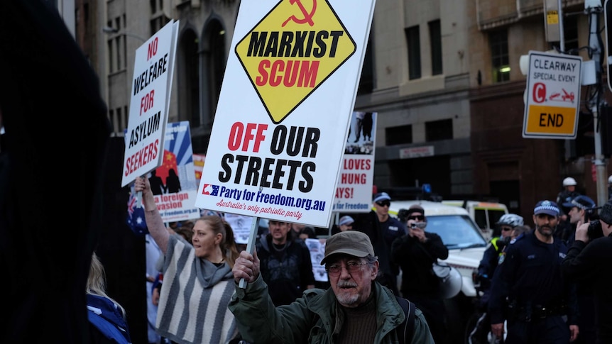 A man holding a sign which reads "Marxist Scum off our streets".