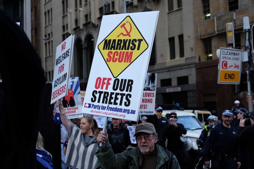 A man holding a sign which reads "Marxist Scum off our streets".