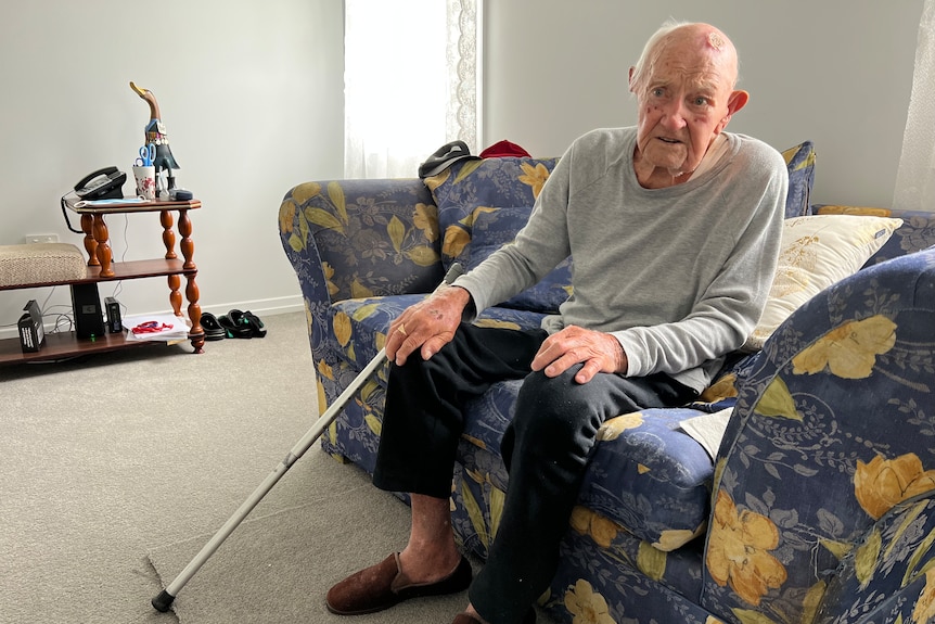 An elderly gentleman sits on a lounge suit with his walking cane beside him