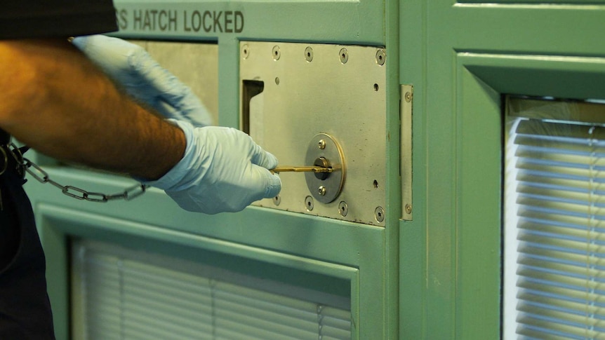 Security staff wearing rubber gloves places a key into a locked door.