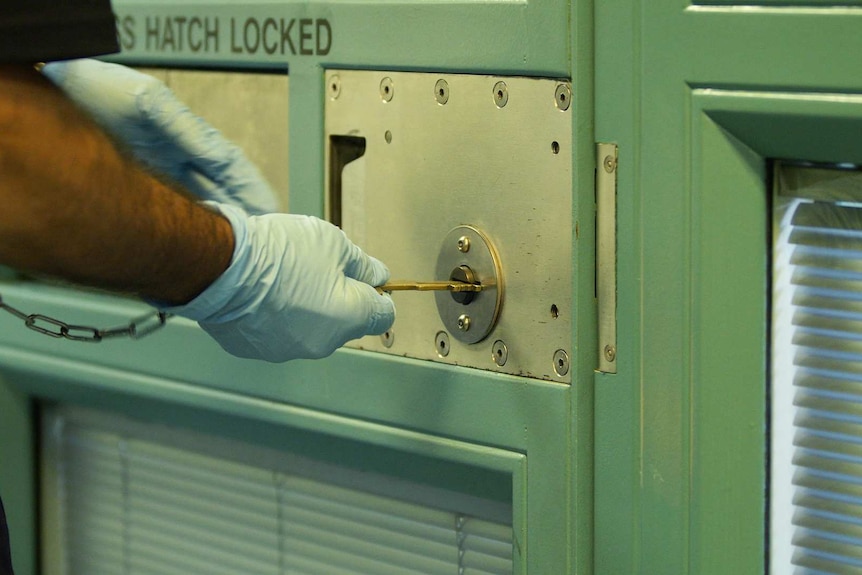 Security staff wearing rubber gloves places a key into a locked door.