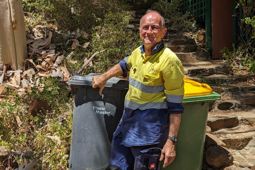 Gerry Lavell stands in front of his landfill wheelie bin smiling and with his thumbs down. 
